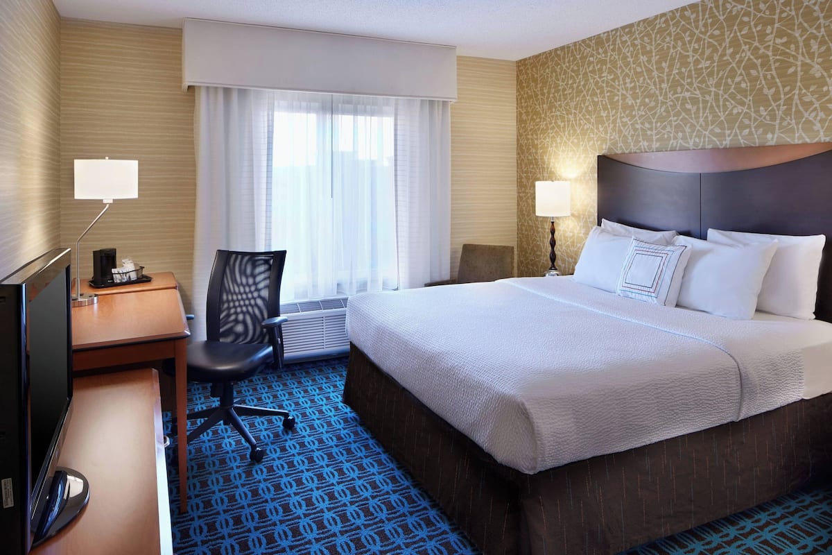 A hotel room with a large bed, a desk with a computer, a chair, and a window with curtains.