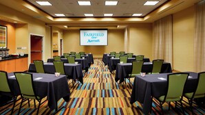 Une salle de conférence équipée de tables et de chaises, d’un écran affichant le logo « Fairfield Inn Marriott » et d’un sol recouvert de moquette.