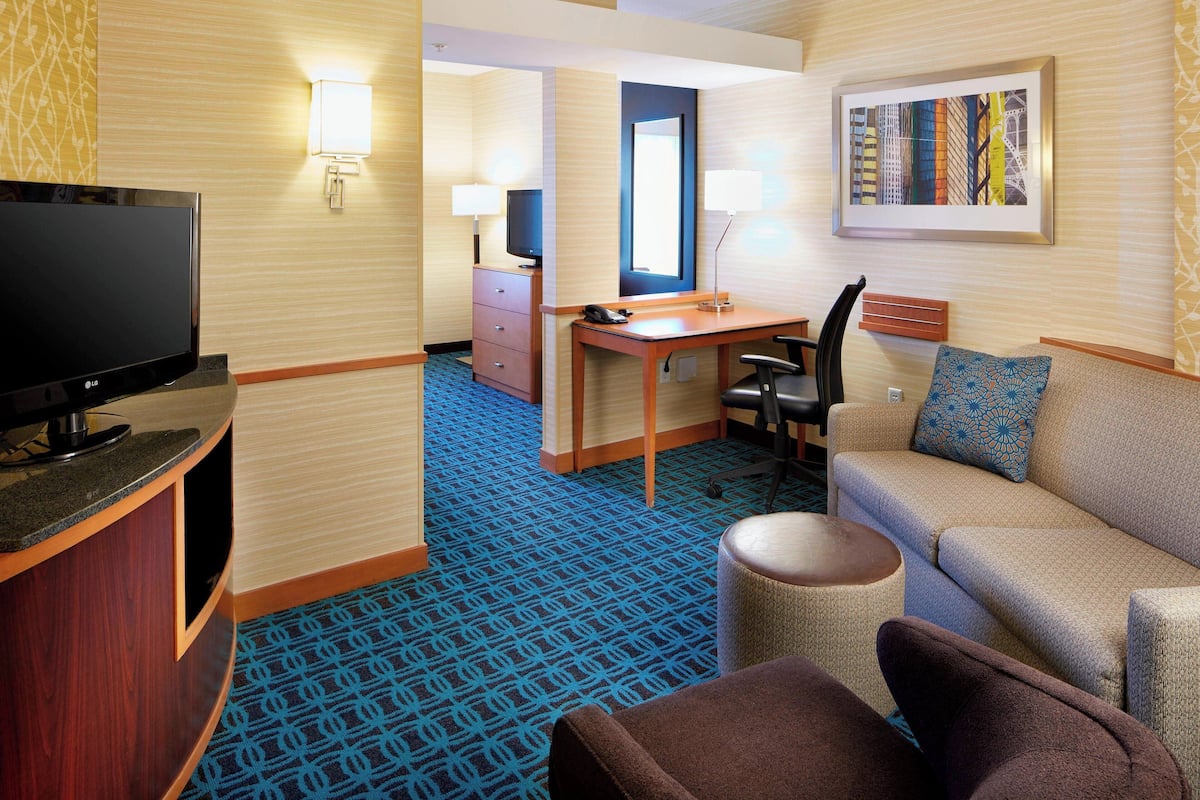 A hotel room with a TV, desk, chair, sofa, and a patterned carpet.