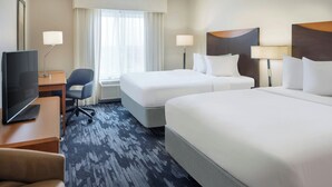 Une chambre d’hôtel avec deux lits, un bureau avec une télévision, une chaise et une fenêtre avec des rideaux.