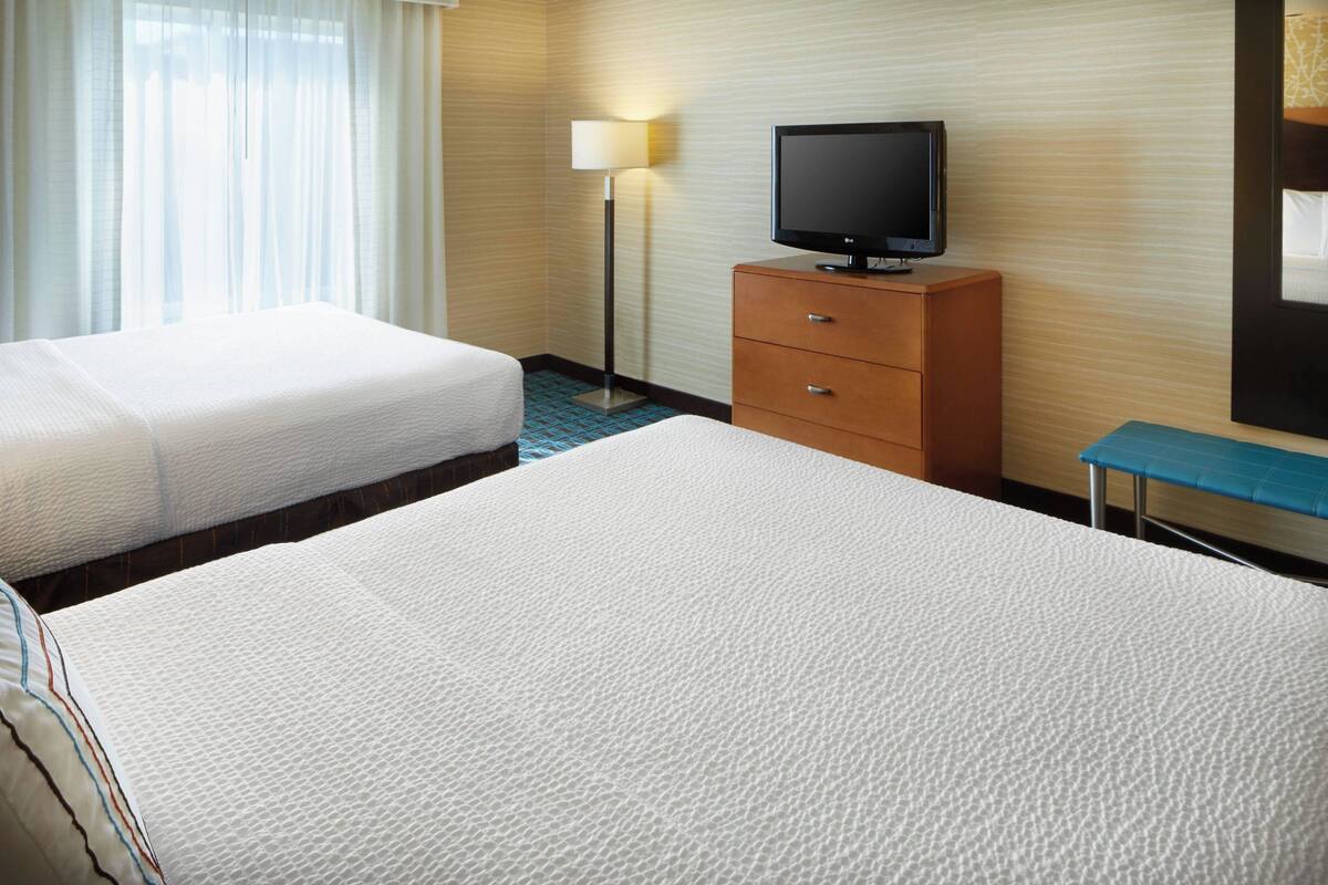 A hotel room with two beds, a television on a wooden dresser, a floor lamp, and a mirror on the wall.