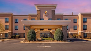 Un hotel Comfort Suites con diseño moderno, que presenta una entrada central, un área de espera cubierta y jardines simétricos.