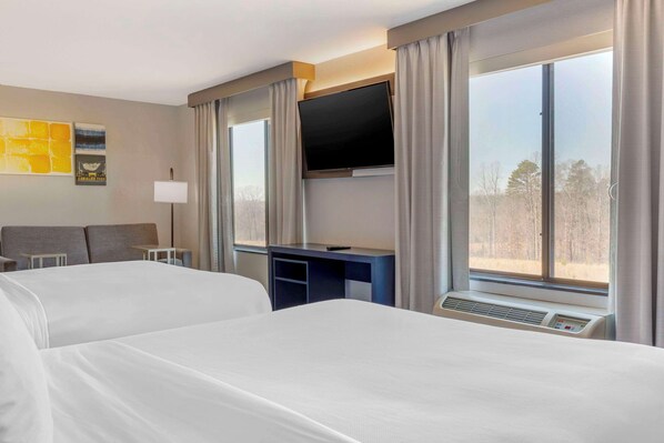 A hotel room with two beds, a desk, a flat-screen TV, and large windows with curtains.