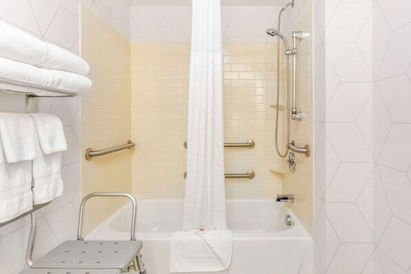 A bathroom with a shower, a bathtub, a step stool, and a towel rack with multiple towels.