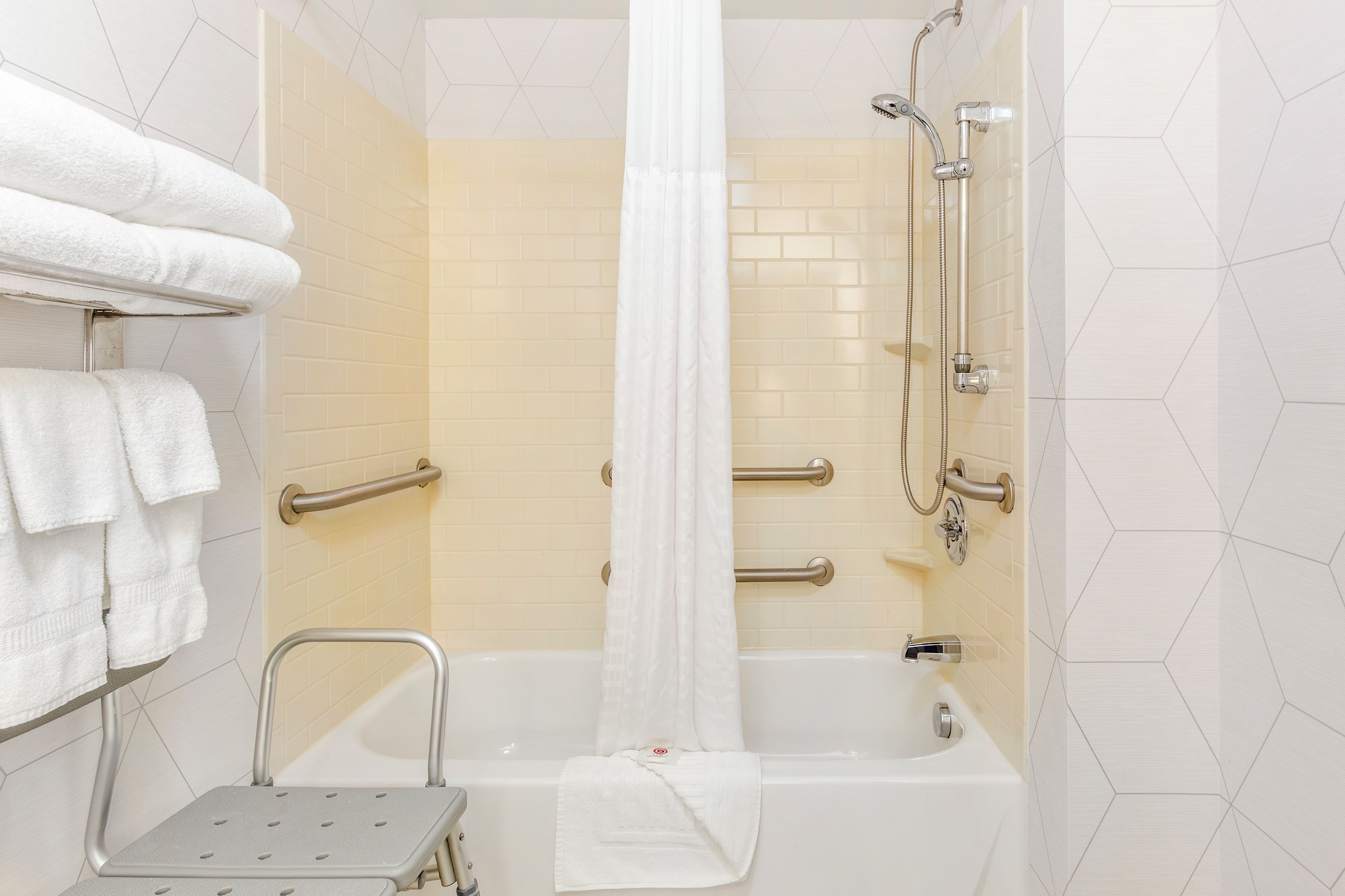 A bathroom with a bathtub, shower, grab bars, and a step stool.