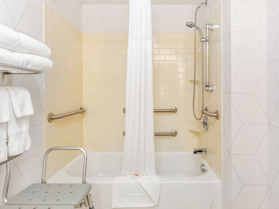Een badkamer met een badkuip, douche, grepen en een opstapje.