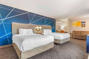 A hotel room with two beds, a sofa, a desk, and a wall with a geometric pattern.