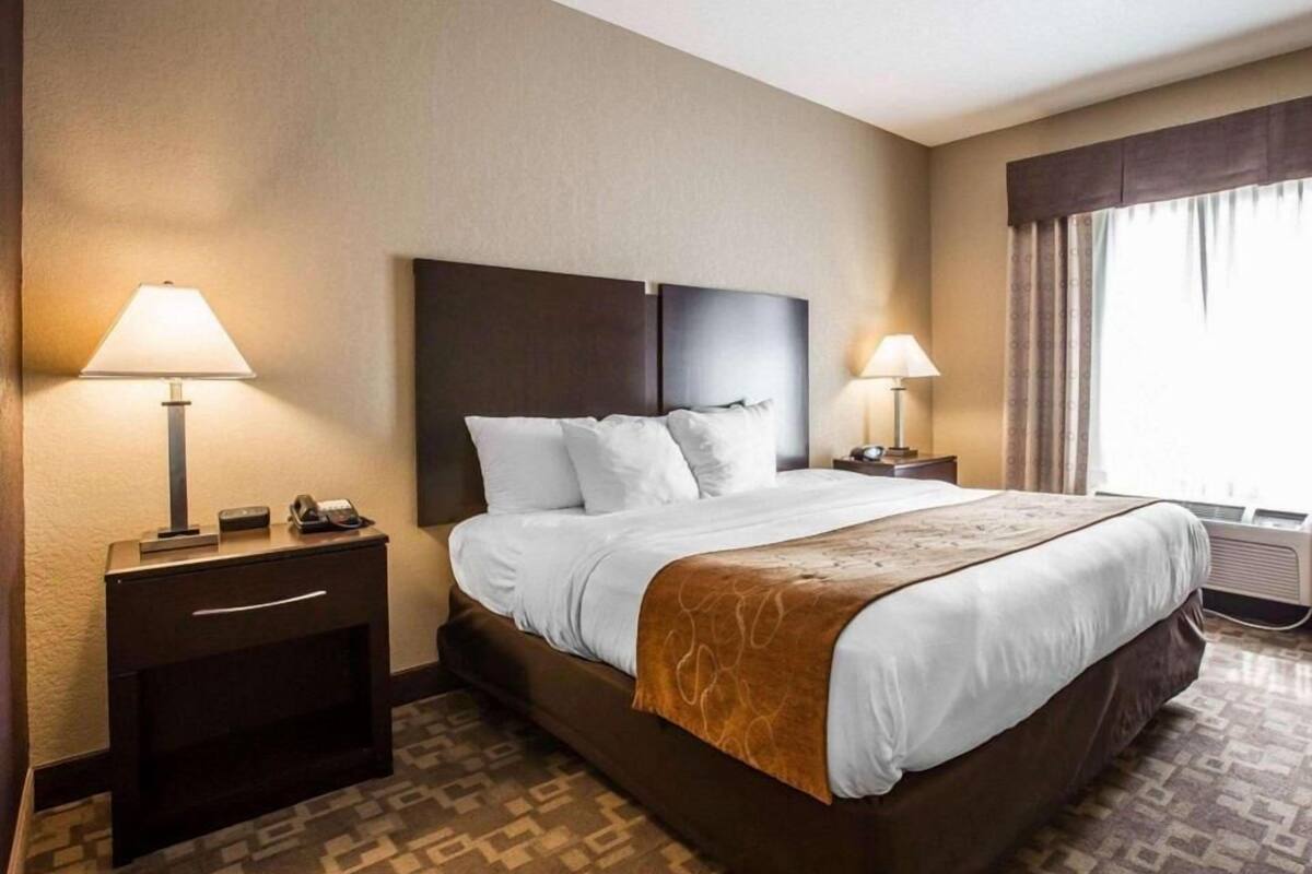 A hotel room with a large bed, two bedside tables with lamps, a telephone, and a window with curtains.