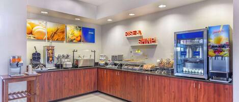 A modern breakfast area with a coffee machine, juice dispenser, and food display.