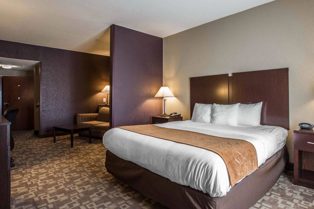 A hotel room with a large bed, a desk, a chair, and a lamp.