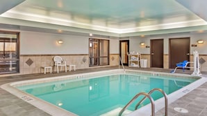 Una piscina con solárium empedrado, un área de descanso con sillas, y una puerta que da a un vestuario.
