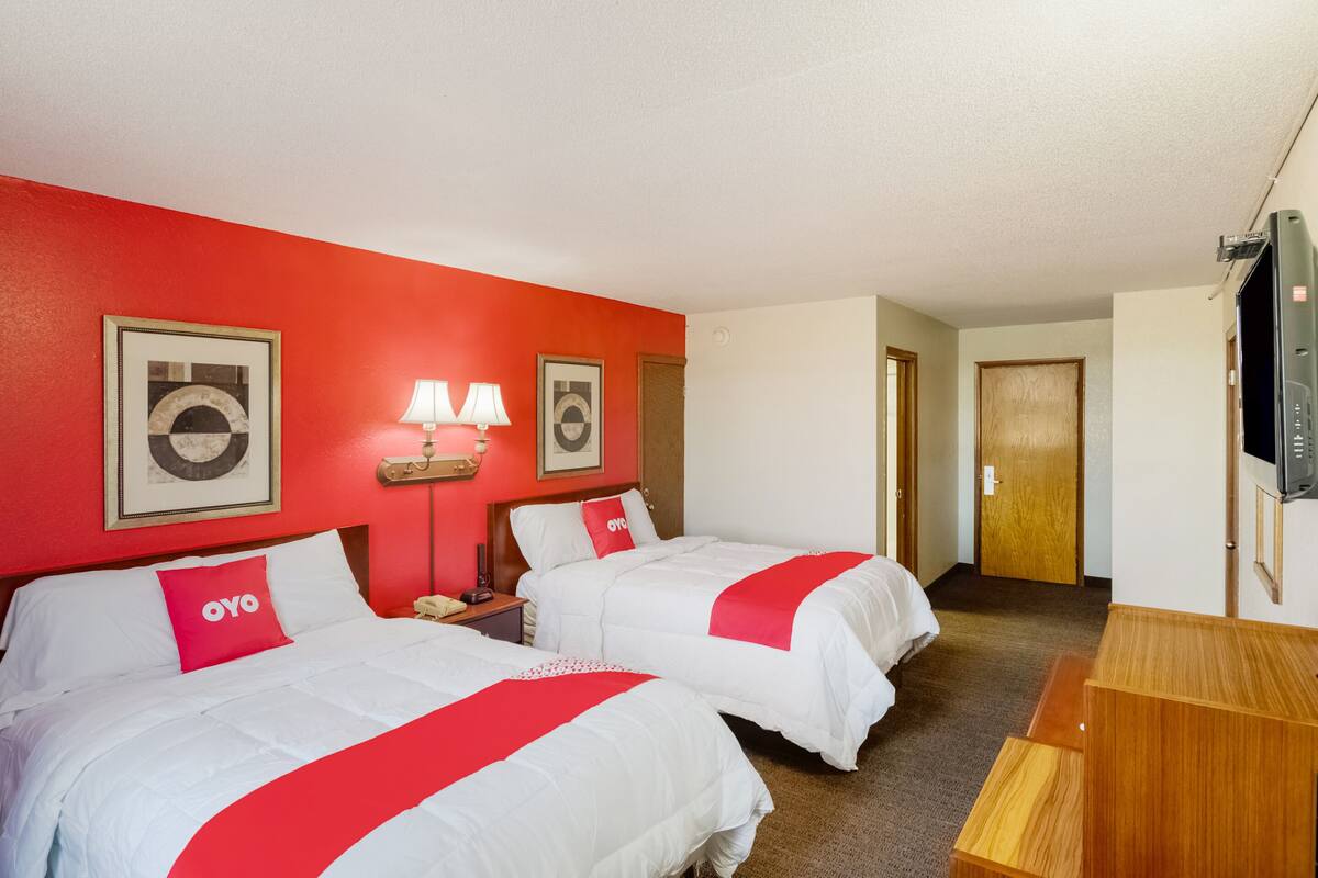 A hotel room with two beds, red walls, and a wooden desk.