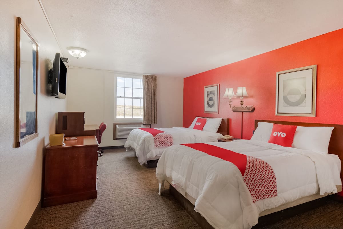 A hotel room with two beds, a desk, a TV, and a window with curtains.