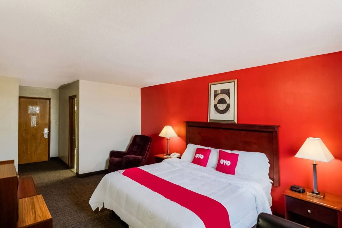 A hotel room with a large bed, two bedside lamps, a chair, and a door.