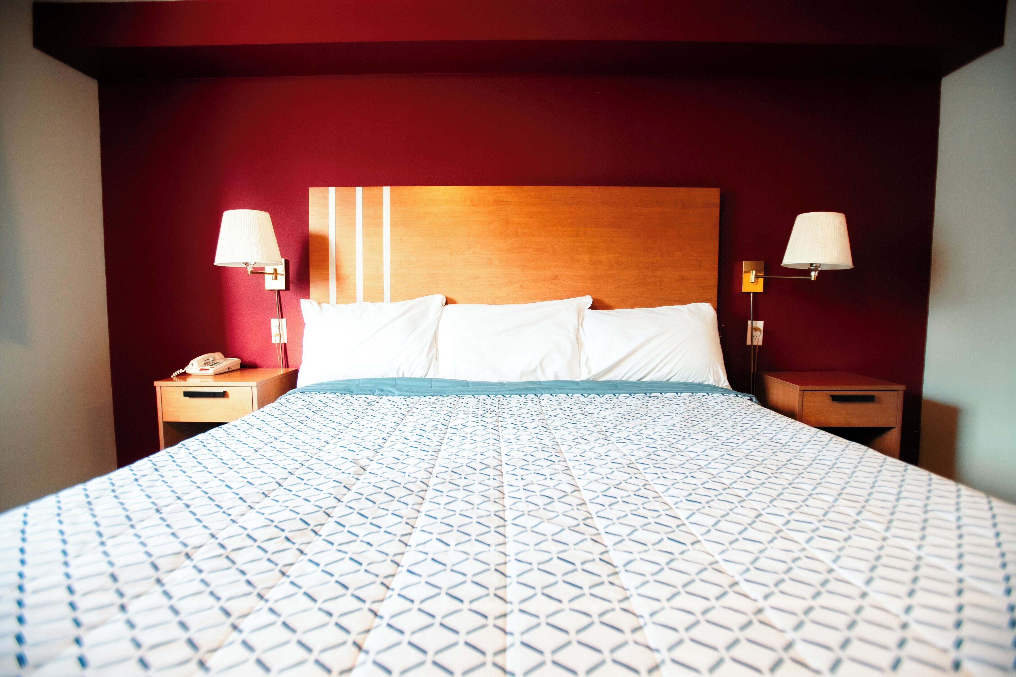 A hotel room with a large bed, two bedside tables, a wooden headboard, and two wall-mounted lamps.
