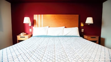 A hotel room with a large bed, two bedside tables, a wooden headboard, and two wall-mounted lamps.