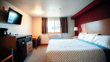 A hotel room with a bed, a desk, a television, and a window with curtains.