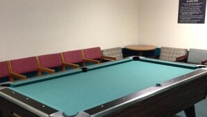 Une table de billard dans une pièce dotée d’une moquette bleue, d’un luminaire suspendu et d’une enseigne fixée au mur.