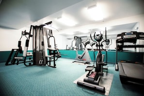 A gym with various exercise machines, a treadmill, and a wall-mounted TV.