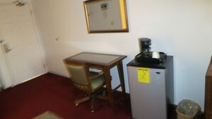 Une petite pièce avec un bureau en bois, une chaise, un réfrigérateur et une porte.