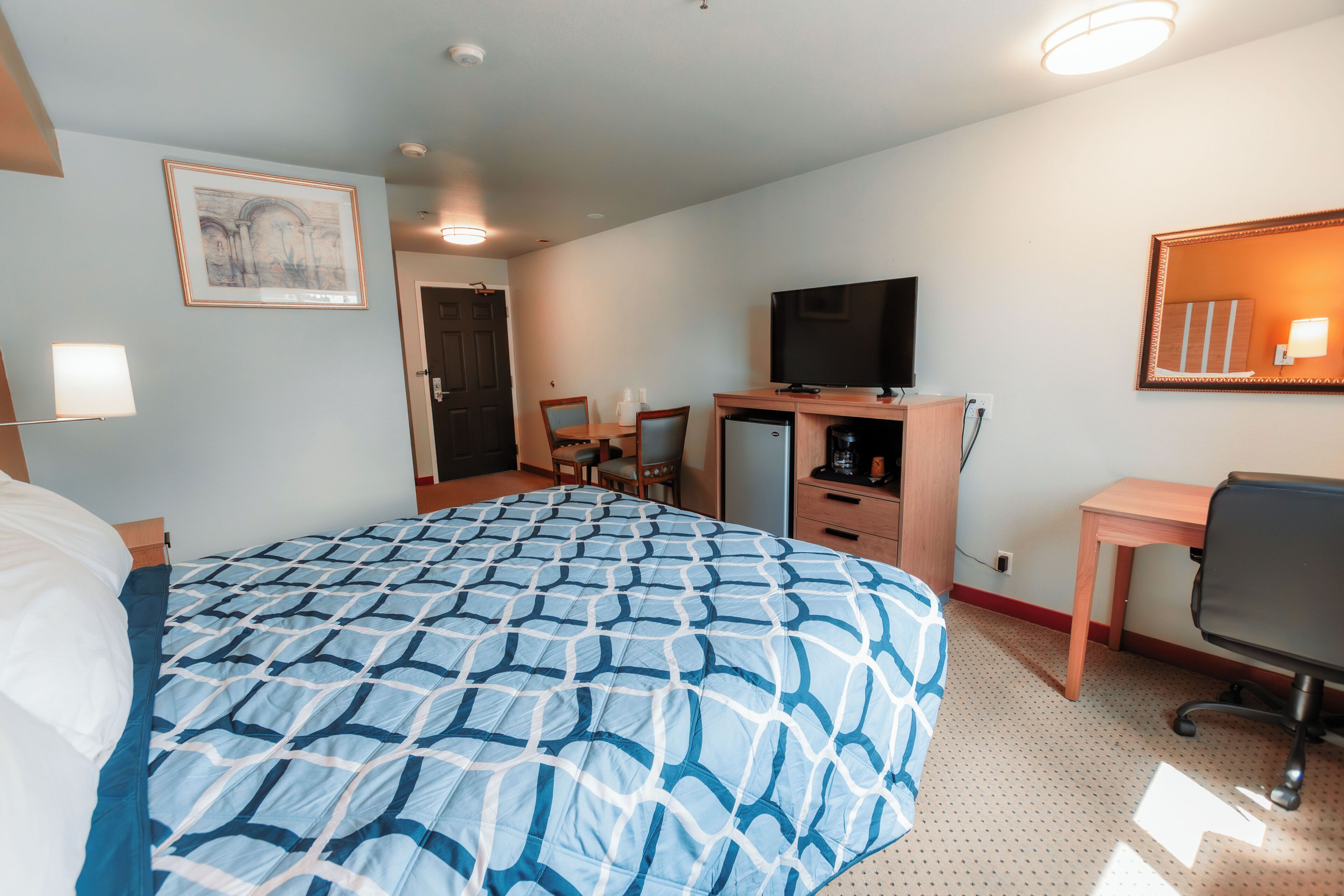 A hotel room with a large bed, a desk, a television, and a small refrigerator.