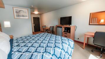 A hotel room with a large bed, a desk, a television, and a small refrigerator.