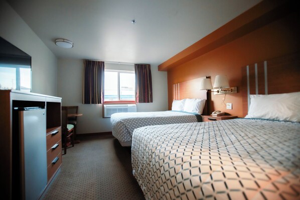A hotel room with two beds, a desk, a wardrobe, and a window with curtains.
