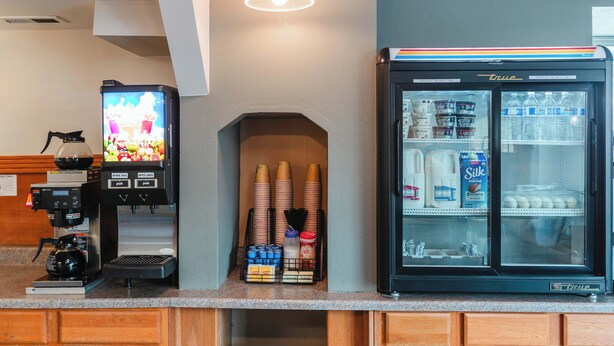 Une machine à café, un distributeur de boissons et un réfrigérateur rempli de lait et de diverses boissons.