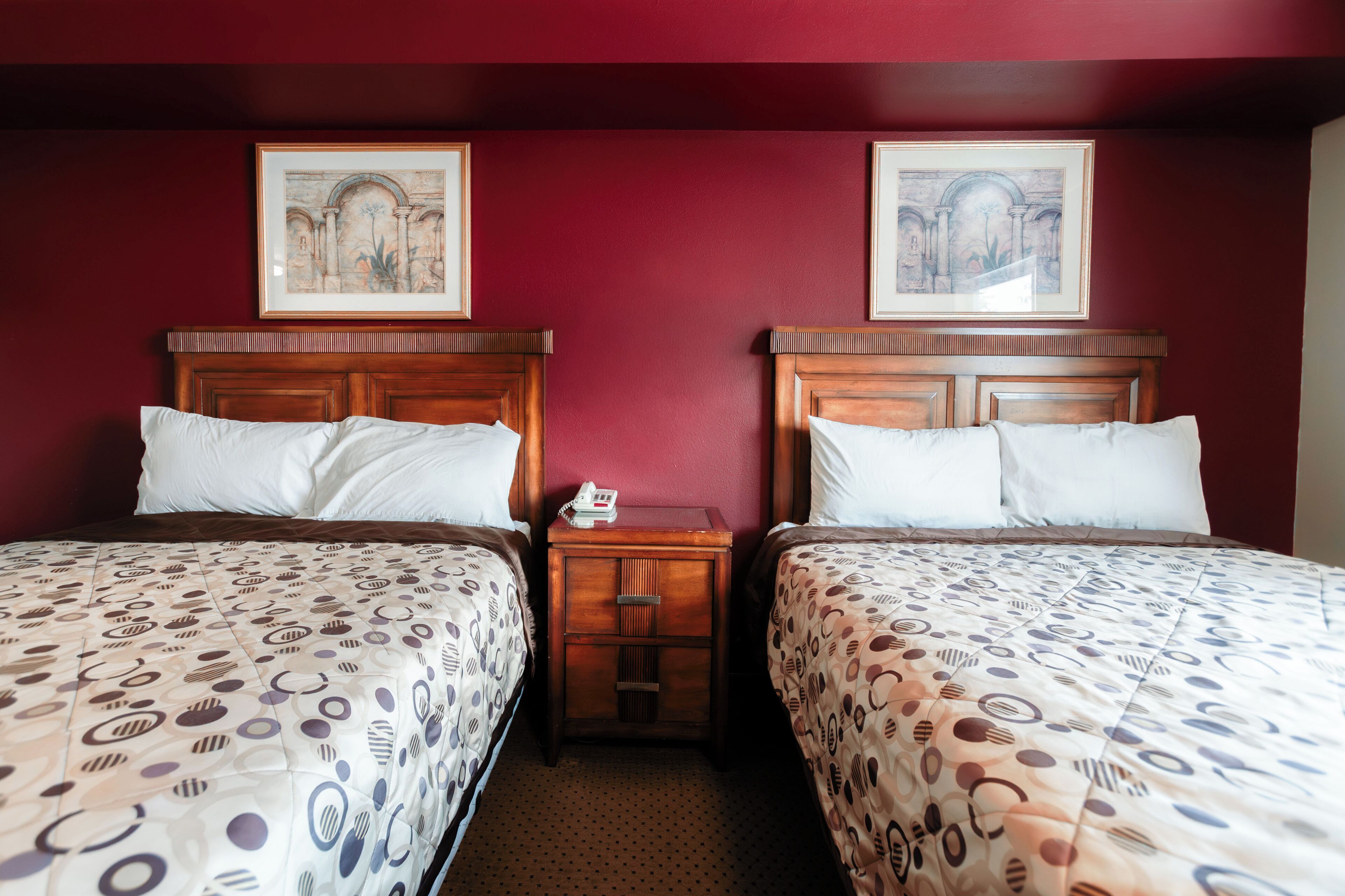 Une chambre d’hôtel avec deux lits, une table de chevet avec un téléphone et deux tableaux encadrés au mur.