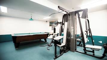 Een sportschool met trainingsapparatuur, een pooltafel en een plafondlamp.