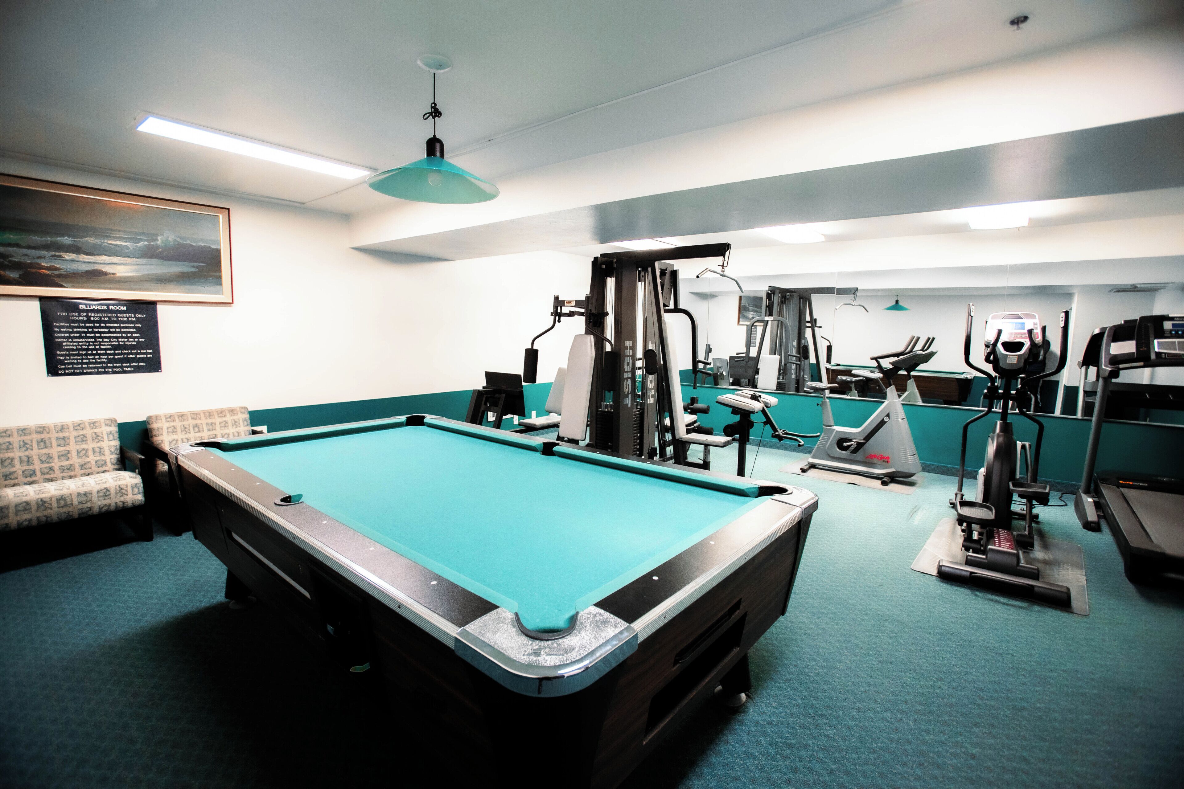 Una sala de billar con mesa de pool, equipo de ejercicio y zona de estar.