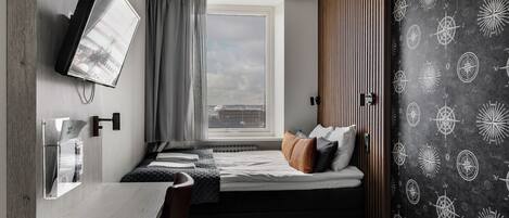 Una habitación pequeña con cama, escritorio, televisión y ventana con cortinas.