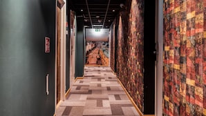 Un pasillo con alfombra estampada, paredes oscuras y un mural de colores.
