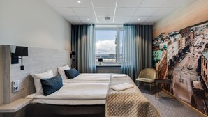 Une chambre d’hôtel avec un grand lit, une vue sur le paysage urbain par la fenêtre et une fresque représentant la ville sur le mur.