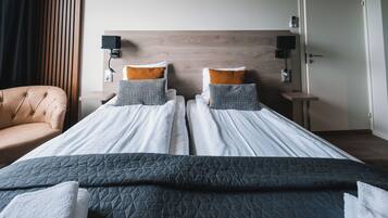 A hotel room with two beds, a wooden headboard, a bedside table with a lamp, and a chair.