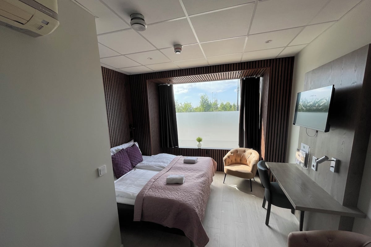 Habitación de hotel con cama, dos sillones, escritorio, televisor y ventana con vista a zonas verdes.