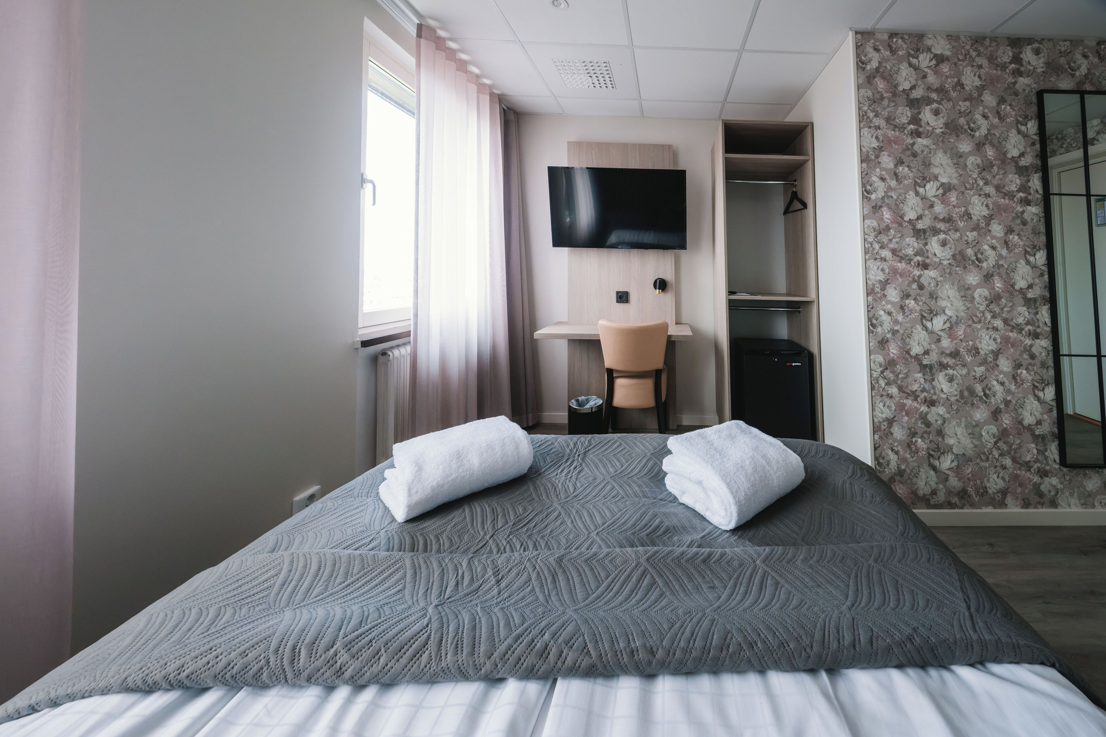 A hotel room with a bed, a TV, a desk, and a shower area.