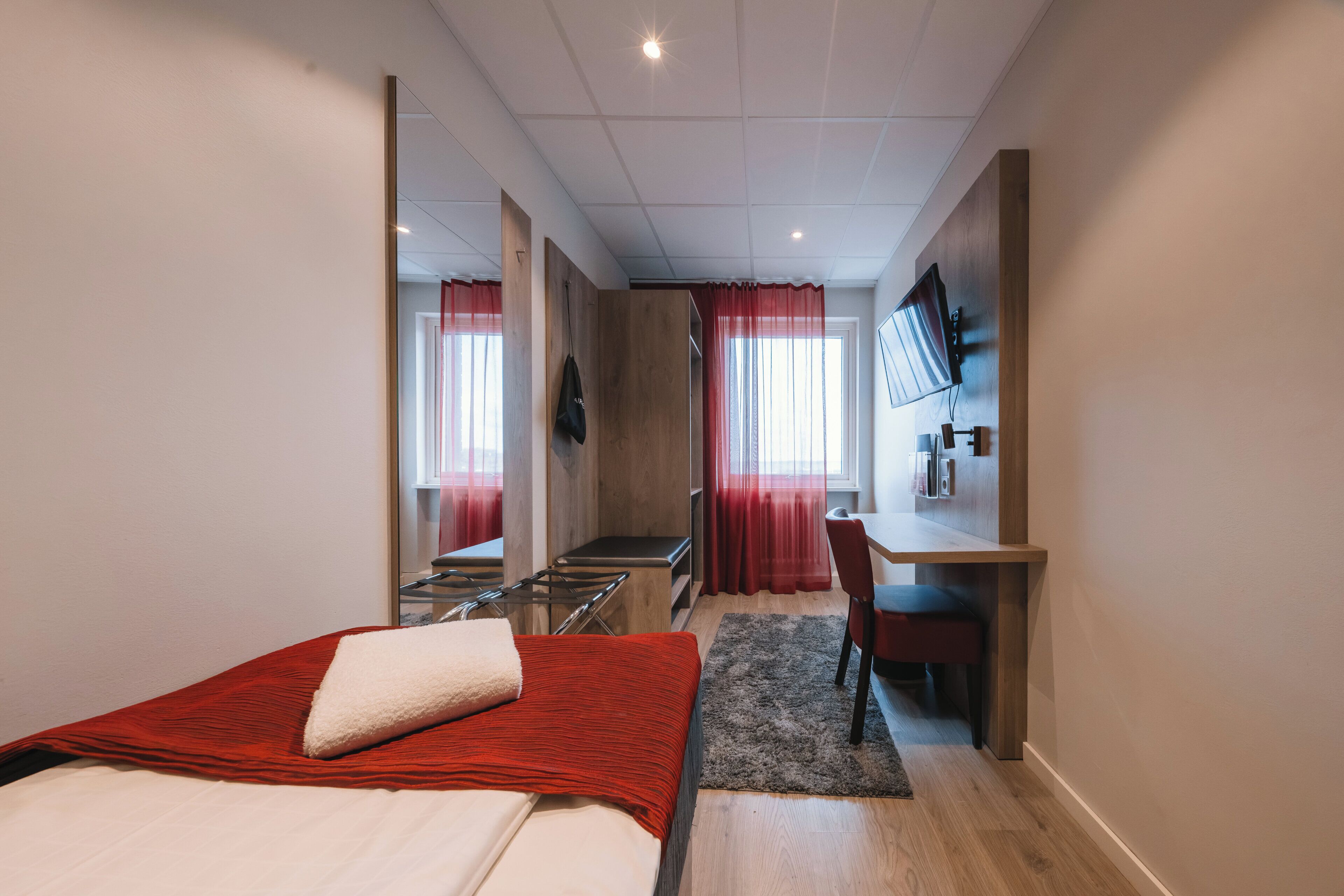 Une chambre d’hôtel équipée d’un lit, d’un bureau, d’une chaise, d’une télévision et d’un miroir.