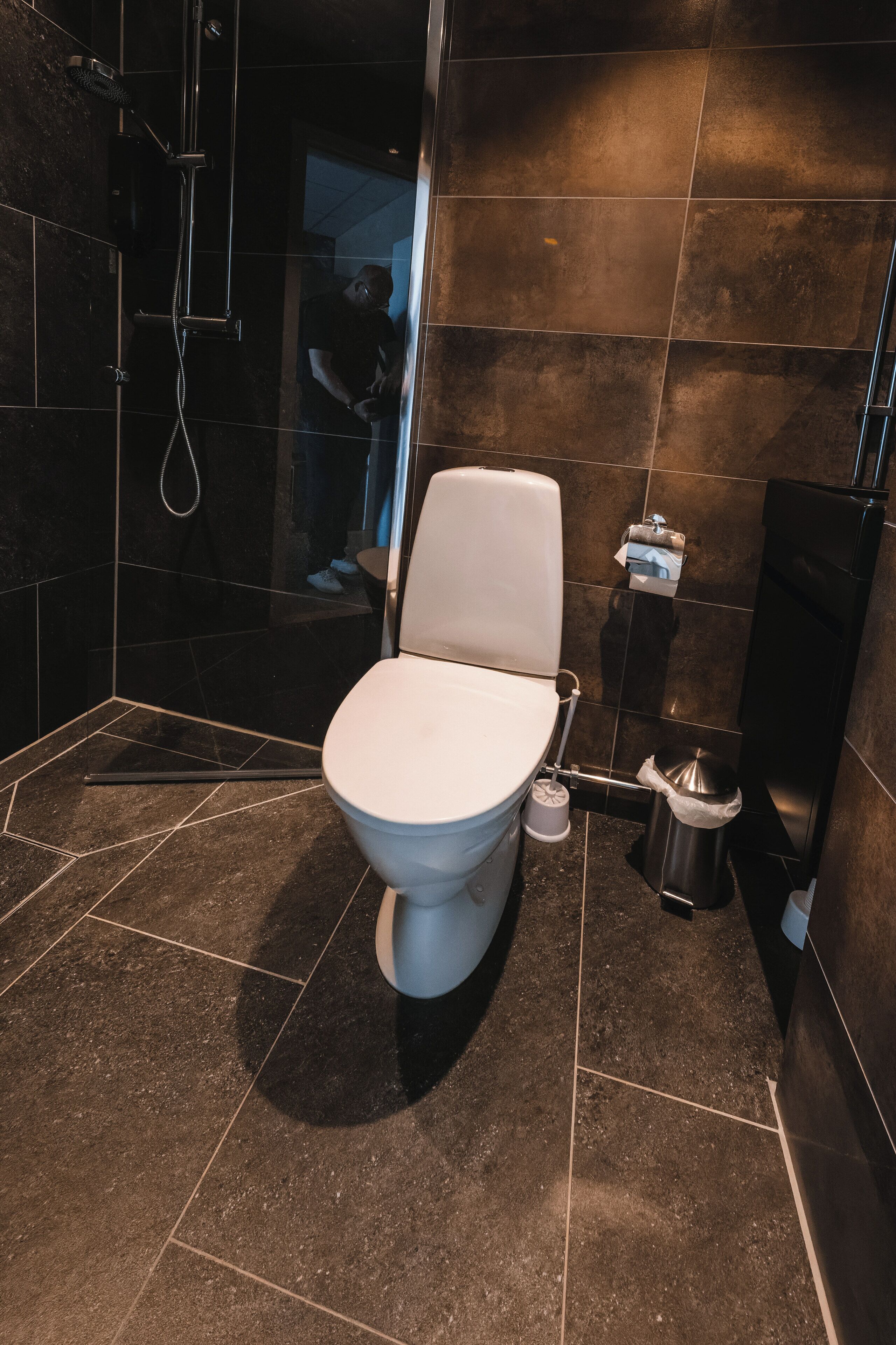 A modern bathroom with a white toilet, a shower area, and a trash bin.
