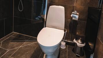A modern bathroom with a white toilet, a shower area, and a trash bin.