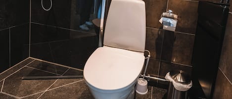 A modern bathroom with a white toilet, a shower area, and a trash bin.