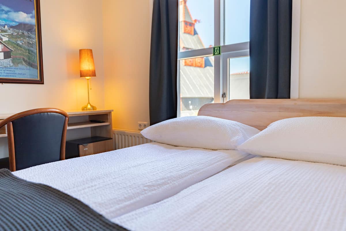 A hotel room with a bed, a desk, a chair, a lamp, and a window with curtains.