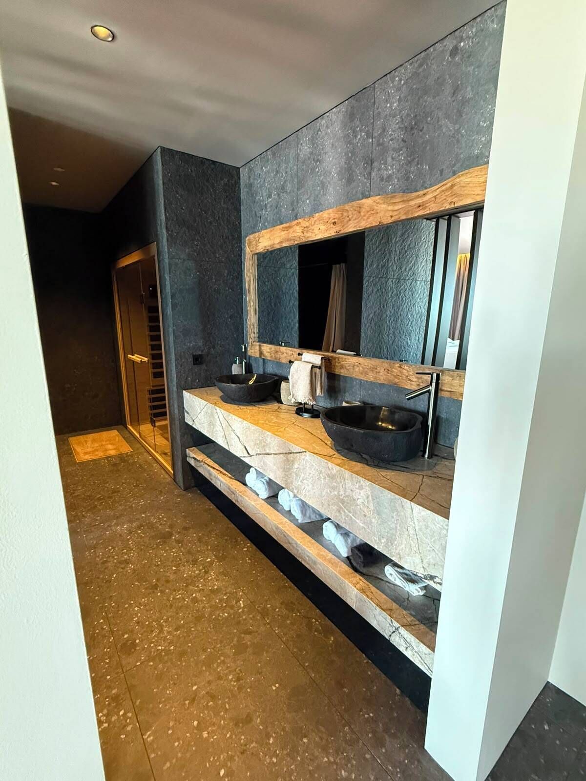 Une salle de bain moderne avec un plan de toilette en pierre, un miroir encadré en bois et un lavabo noir.