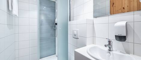 A modern bathroom with a glass-enclosed shower, a white sink, and a wooden cabinet above the mirror.
