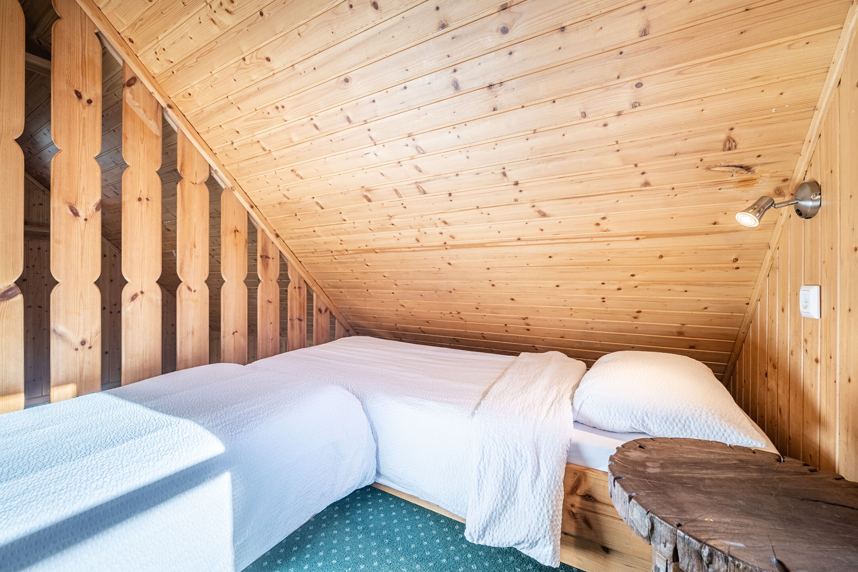 A wooden cabin room with a bed, a wooden bench, and a sloped ceiling.
