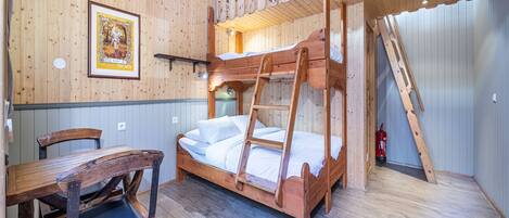 A wooden bunk bed room with a ladder, a wooden table, and a framed picture on the wall.