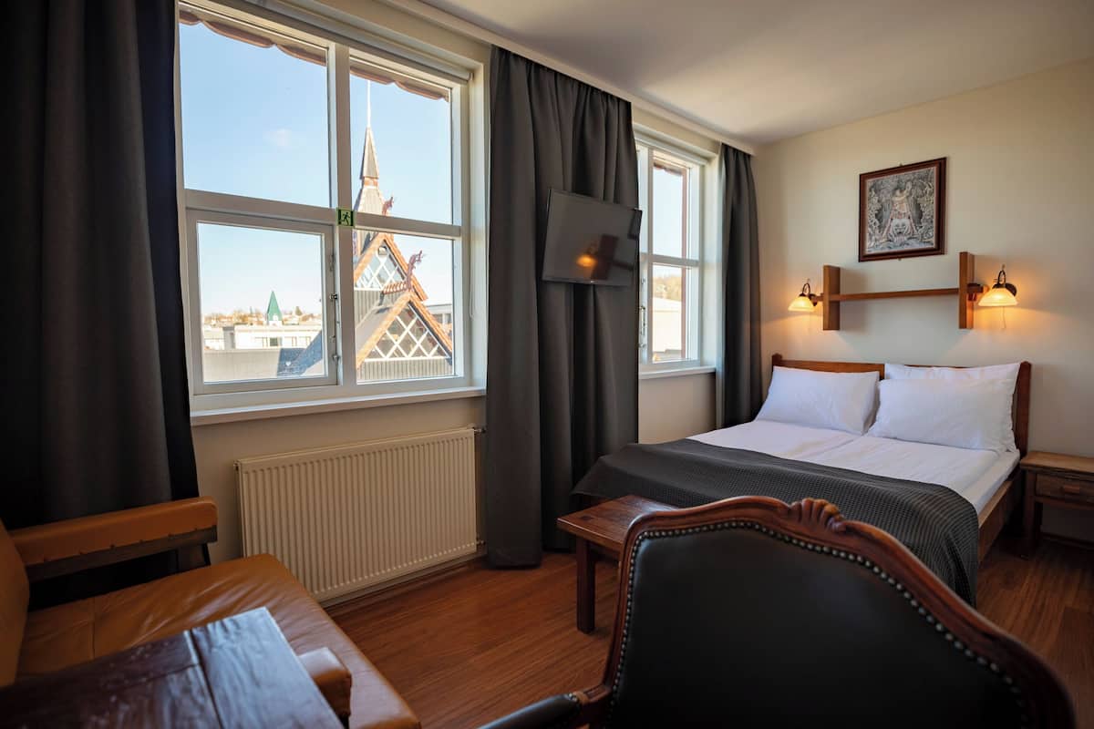 A hotel room with a bed, a desk, a chair, and a window with a view of a building.