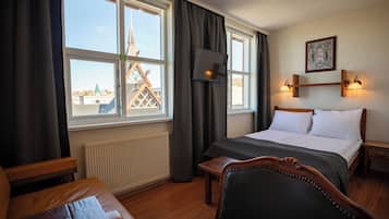 Quarto de hotel com cama, escrivaninha, cadeira e janela com vista para um edifício.