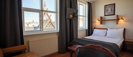 A hotel room with a bed, a desk, a chair, and a window with a view of a building.