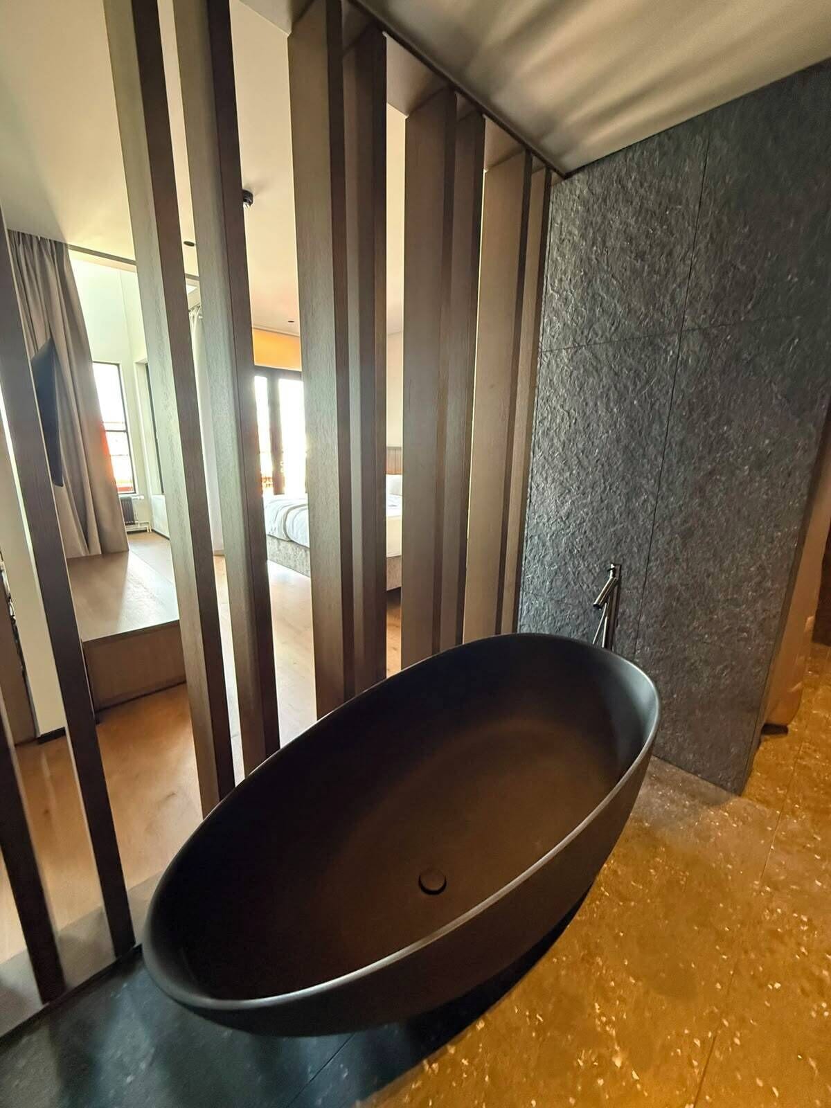 A modern bathroom with a freestanding bathtub, a stone wall, and a view of the adjacent room.